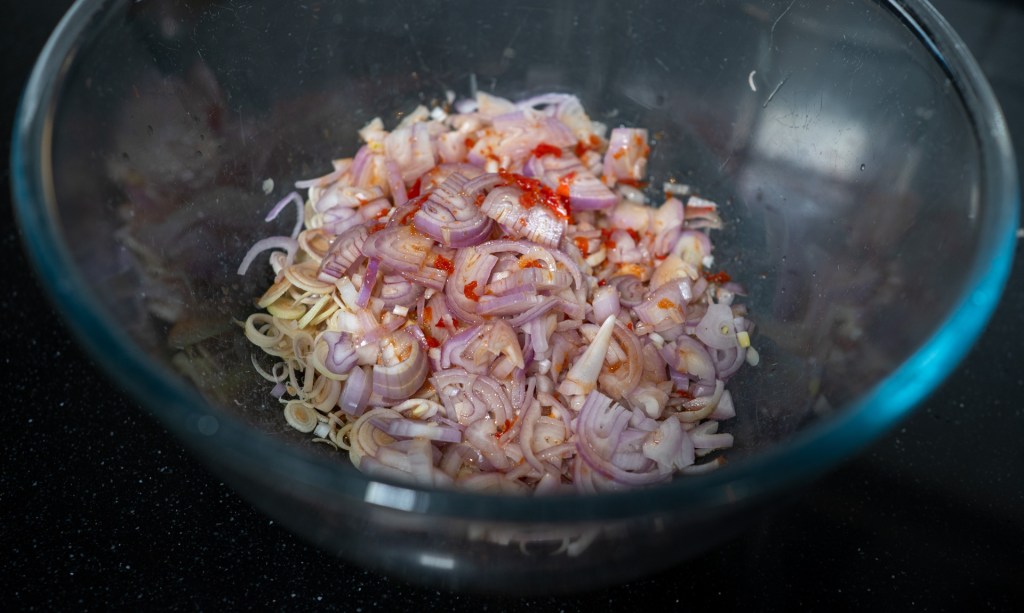 Chopped shallots and lemongrass mixed with chili powder in a glass bowl.