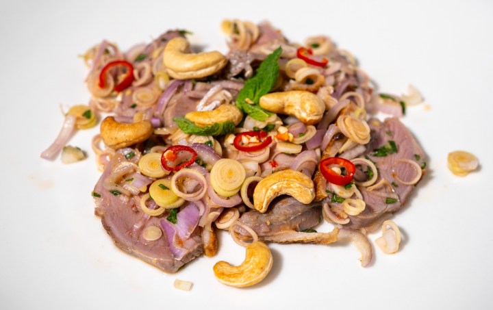 A colorful dish featuring sliced meat topped with herbs, cashews, and red chilies, arranged on a white plate.