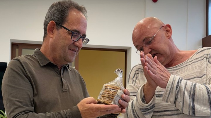 Two men are engaging in conversation while examining a package of crackers.