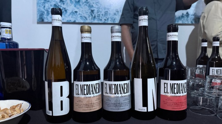 A display of five wine bottles with distinct labels on a table, featuring the names 'EL MEDIANERO' and 'LB' prominently, along with additional wine bottles in the background.