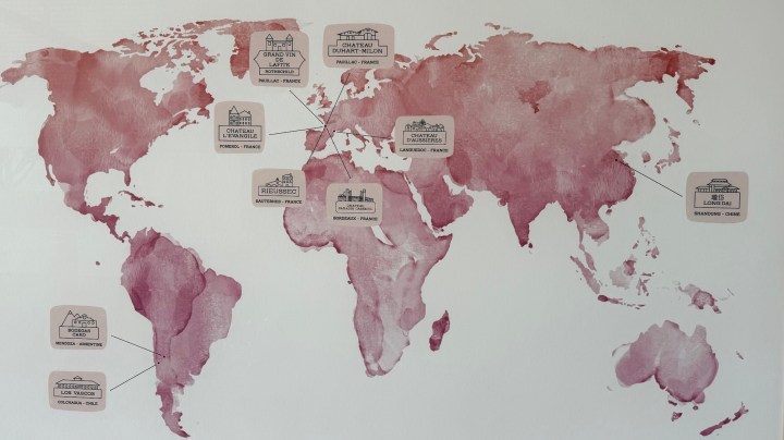 A world map featuring a watercolor design in shades of red, with various locations marked by labeled pins. Each pin indicates a different establishment with corresponding names and locations, including places in France and elsewhere.