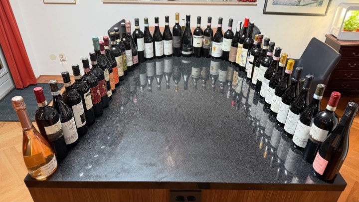 A table featuring an extensive collection of wine bottles arranged neatly around the edge, with various labels and colors, on a black glossy surface.