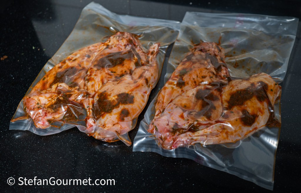 Two vacuum-sealed bags containing marinated chicken breasts, displaying a rich, reddish-brown marinade.