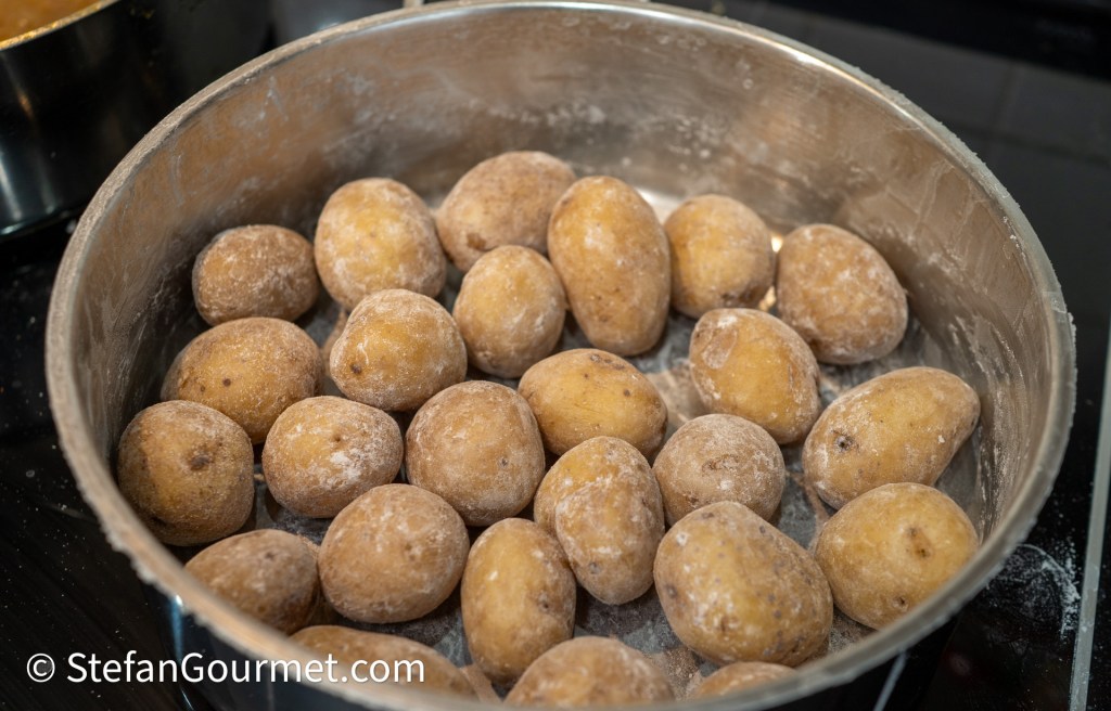A pot filled with unpeeled, slightly dusty raw potatoes, ready for cooking.