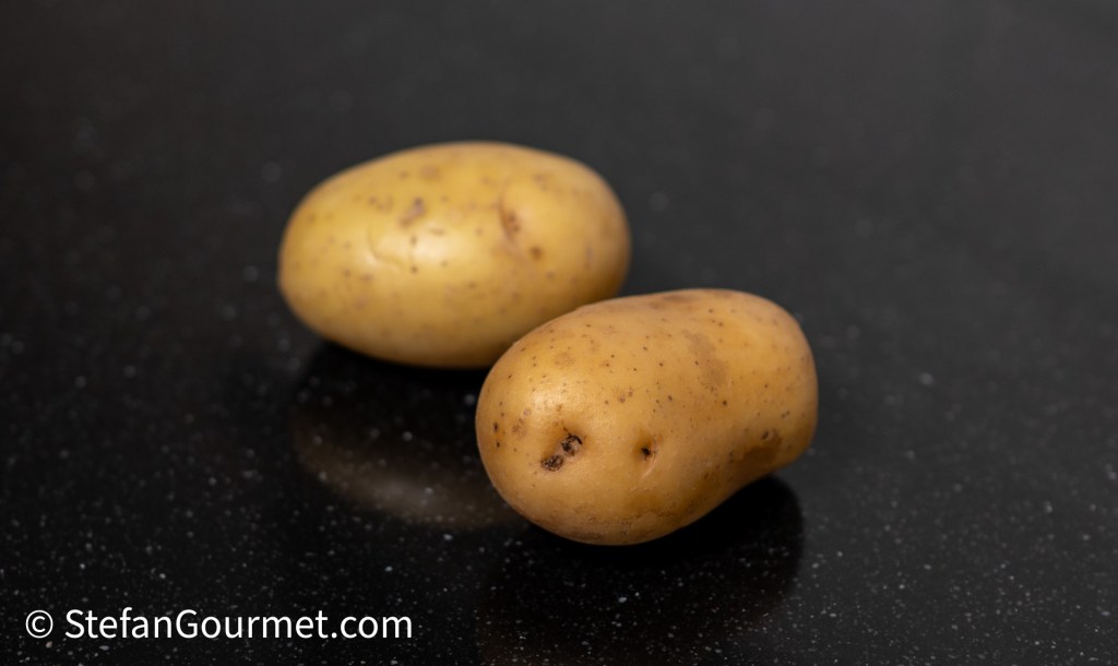 Two brown potatoes on a black countertop