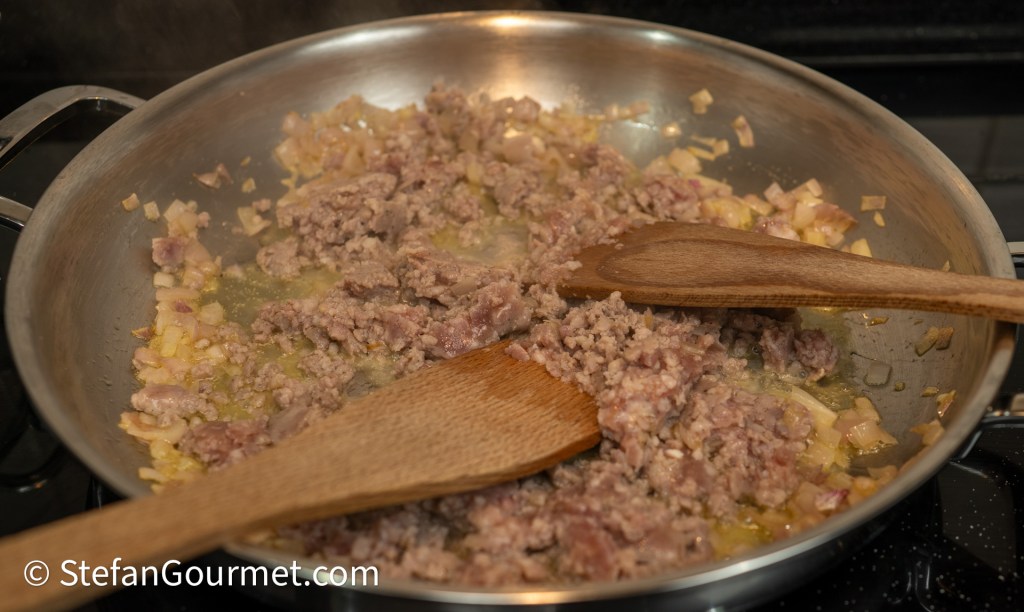 Pan frying ground meat with chopped onions and wooden spatulas in a stainless steel skillet.